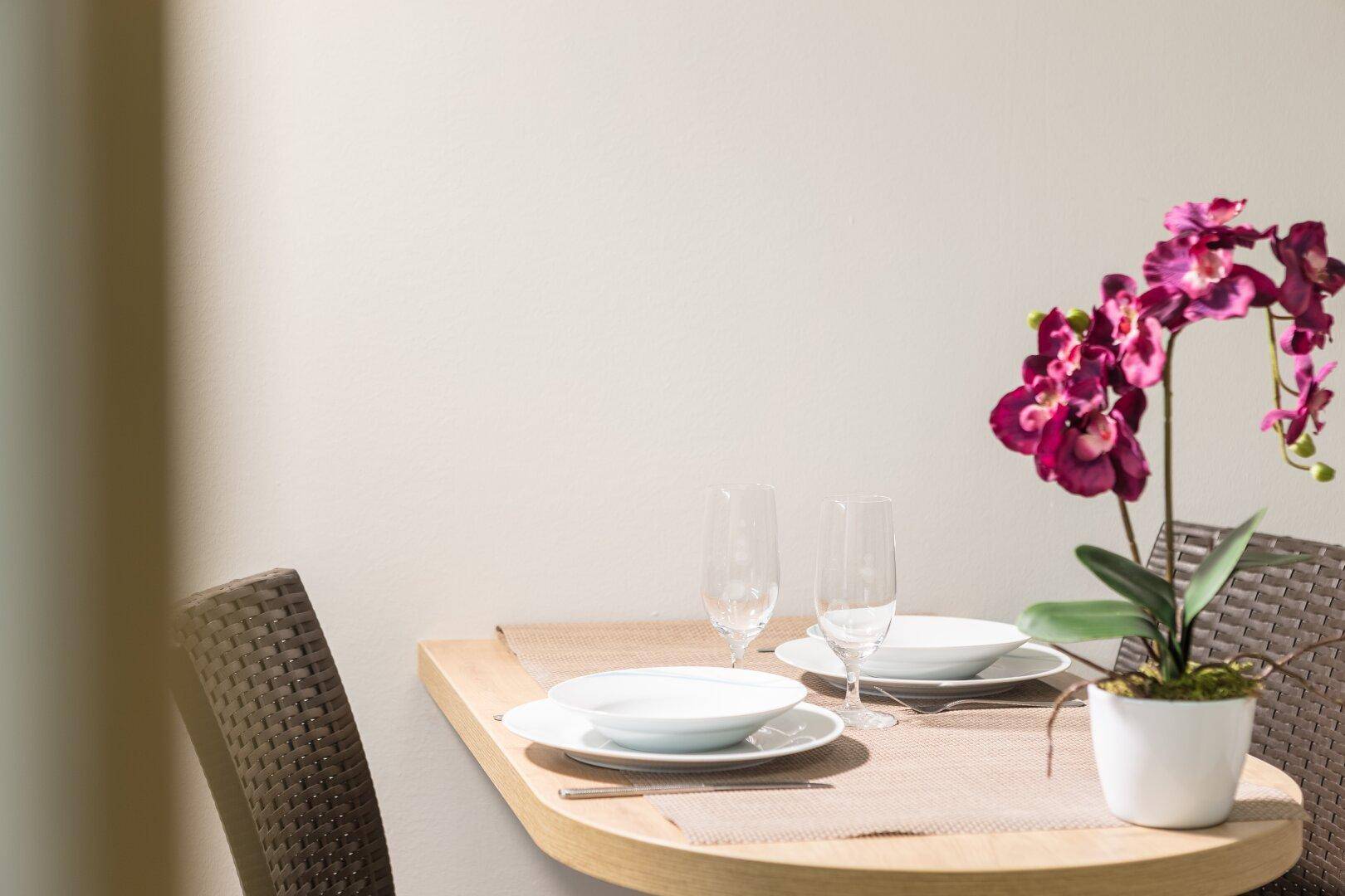 Gedeckter Esstisch für zwei Personen mit dekorativer Orchidee.