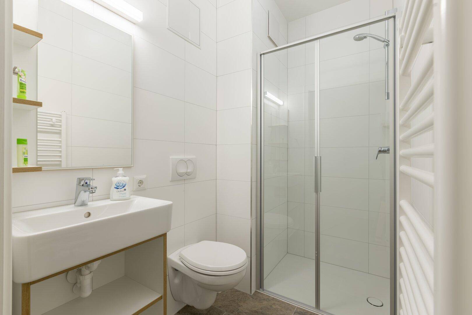 Modernes Badezimmer mit Duschkabine, WC und Waschbecken, hell gefliest.