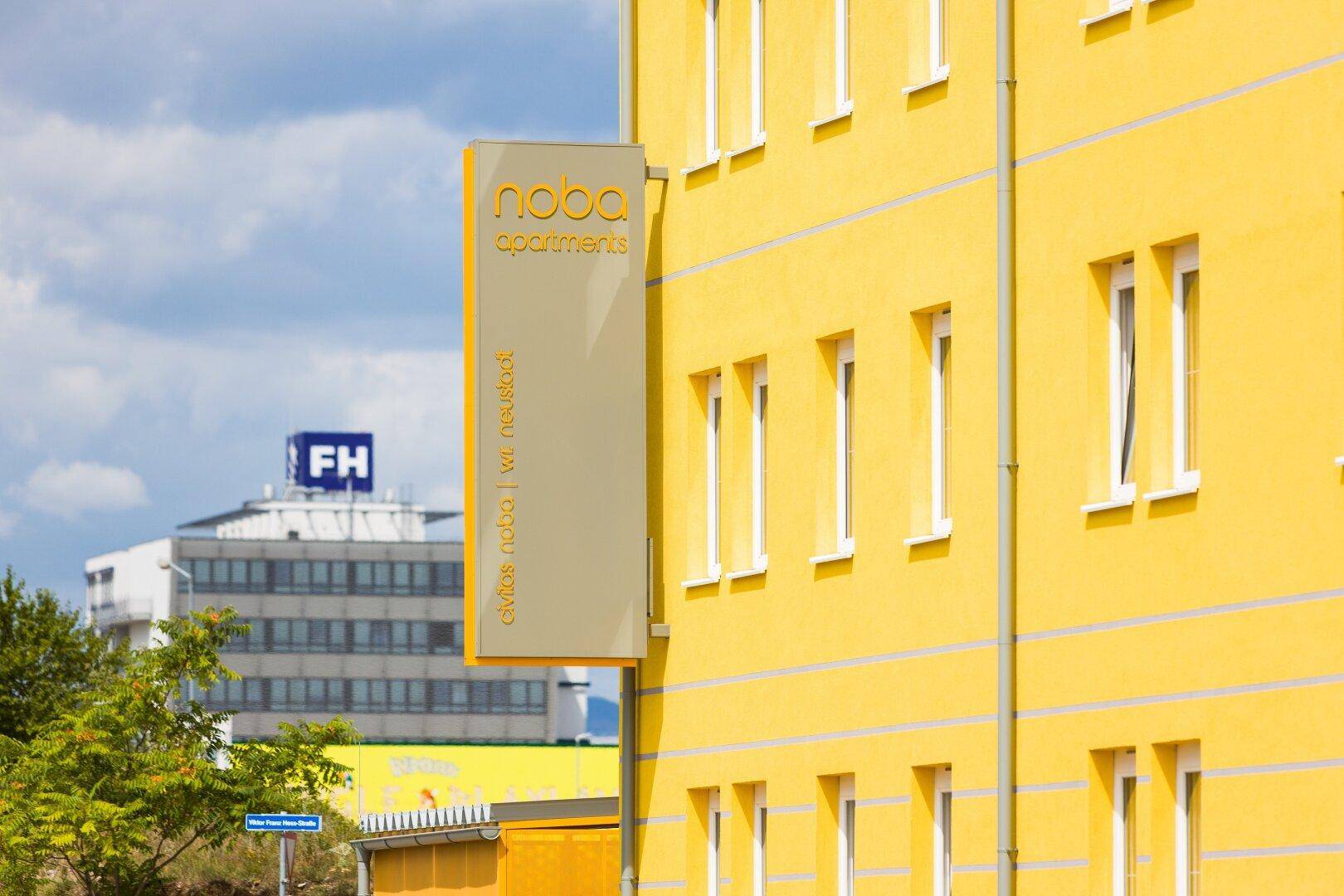 Gelbe Fassade eines modernen Gebäudes mit einem Schild für Noba Apartments.