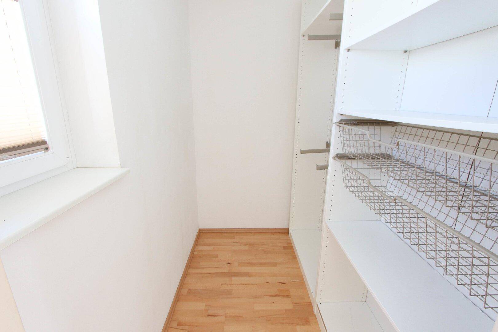 Praktischer begehbarer Kleiderschrank mit Regalsystemen und Fenster für natürliche Belüftung.