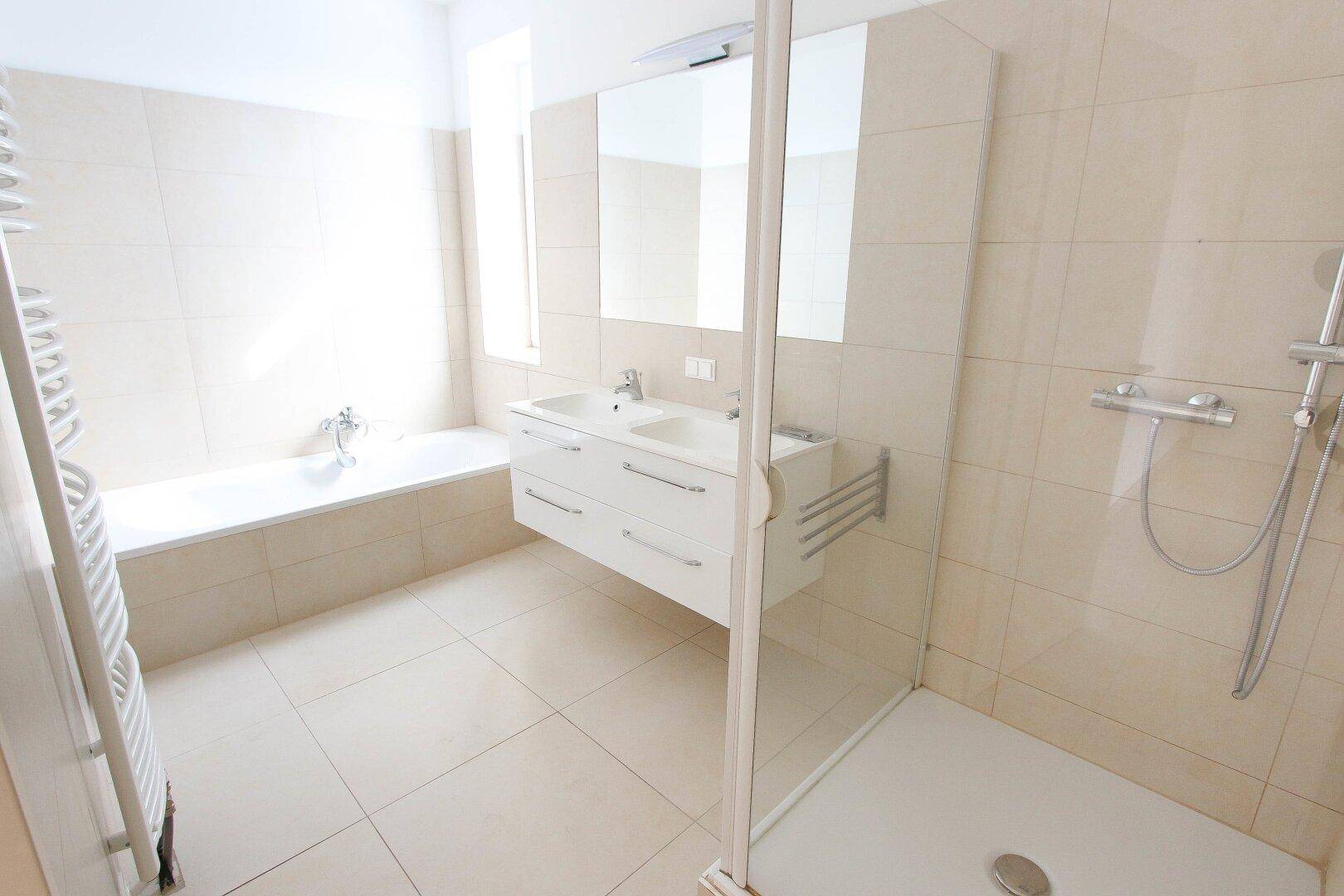 Modernes Badezimmer mit Doppelwaschbecken, Badewanne, Dusche und Handtuchheizkörper.