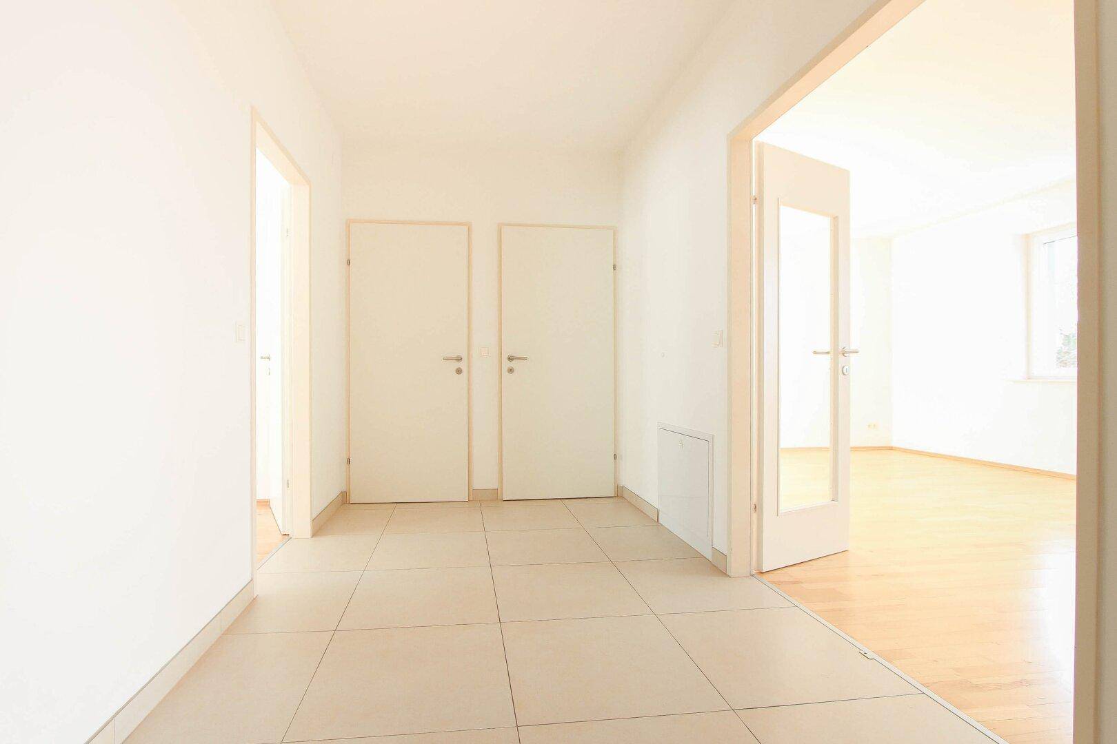 Heller Flur mit Fliesenboden und mehreren Türen, der verschiedene Räume verbindet.