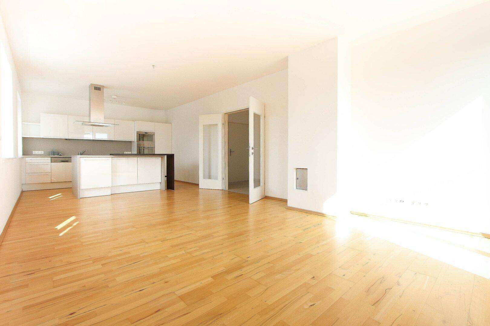 Lichtdurchfluteter offener Wohnbereich mit Holzboden und Zugang zu weiteren Räumen.