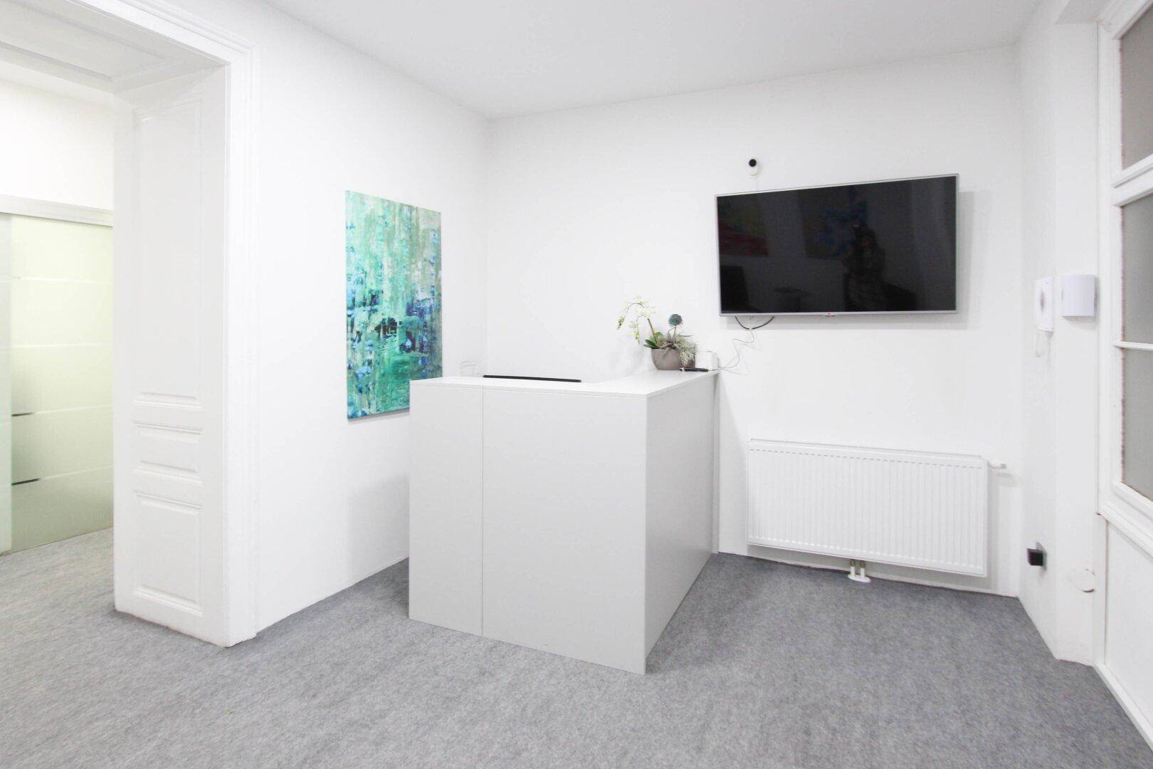 Moderner Empfangstresen in Weiß mit einem Wandfernseher und einem Heizkörper darunter.