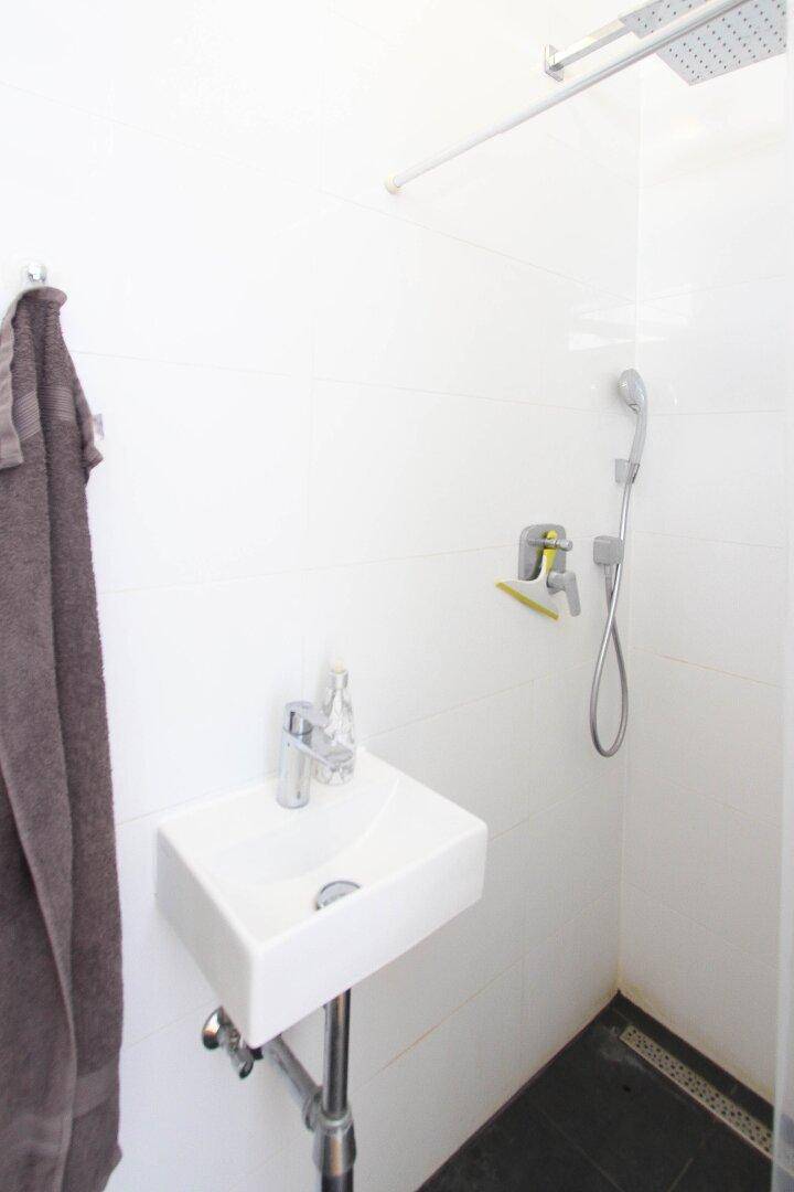 Modernes Badezimmer mit weiß gefliesten Wänden, ebenerdiger Dusche und kleinem Waschbecken.