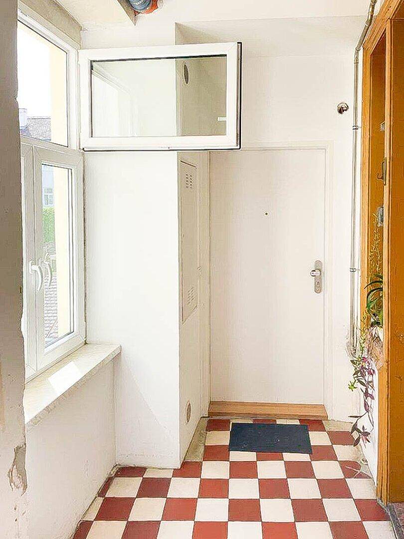 Eingangsbereich mit rot-weiß kariertem Fliesenboden und Fenster, das viel Licht hereinlässt.