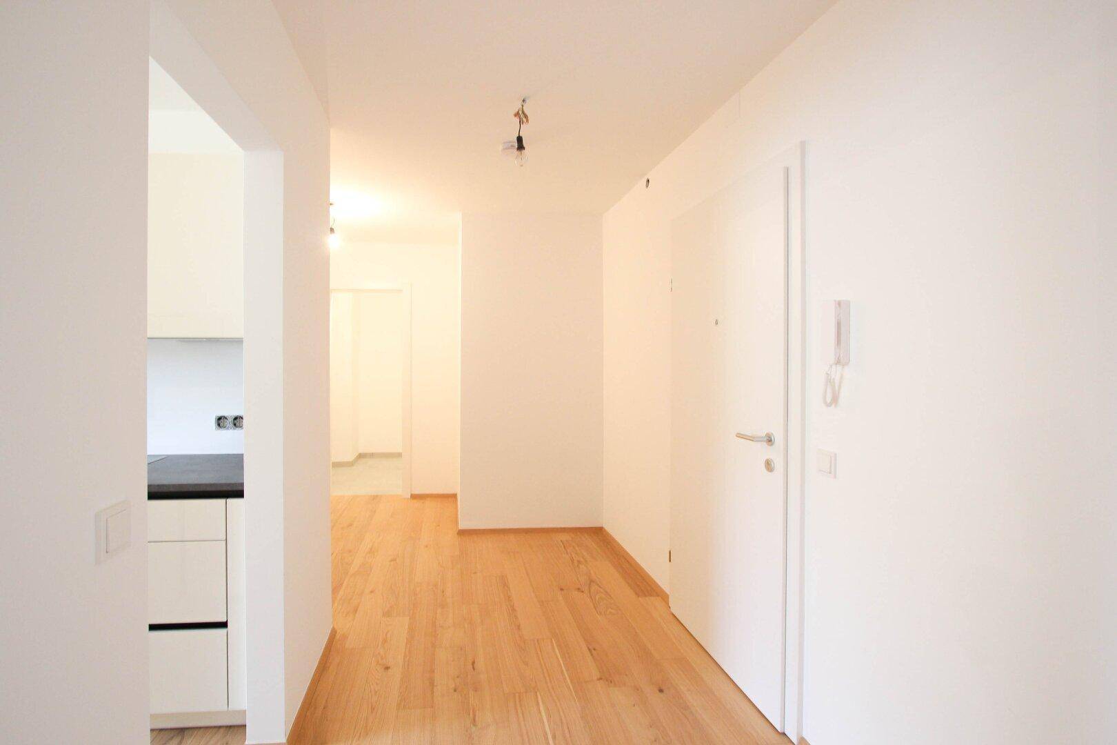 Heller Flur mit neuem Holzboden, weißen Wänden und Zugang zu weiteren Räumen, inklusive einem Blick in die Küche.