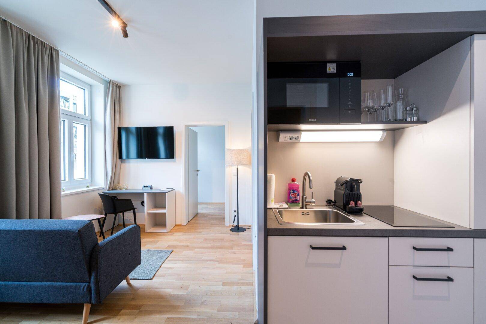 Offener Wohnbereich mit Sofa, Schreibtisch und integrierter Küchenzeile, ideal für modernes Wohnen.