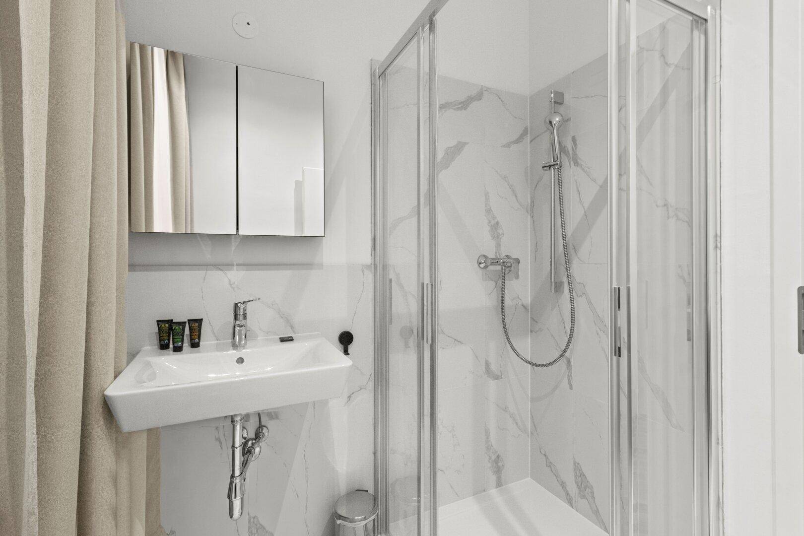 Modernes Badezimmer mit Duschkabine und Waschbecken, ausgestattet mit hellen Marmorfliesen.