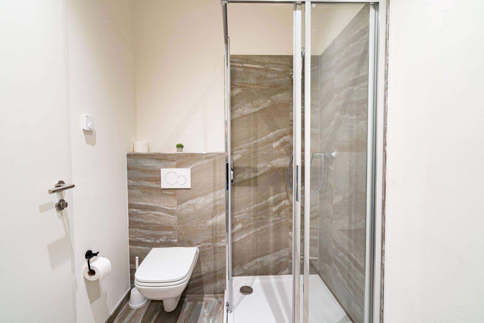 Kleines Badezimmer mit Duschkabine und wandhängendem WC, modern gefliest und funktional.
