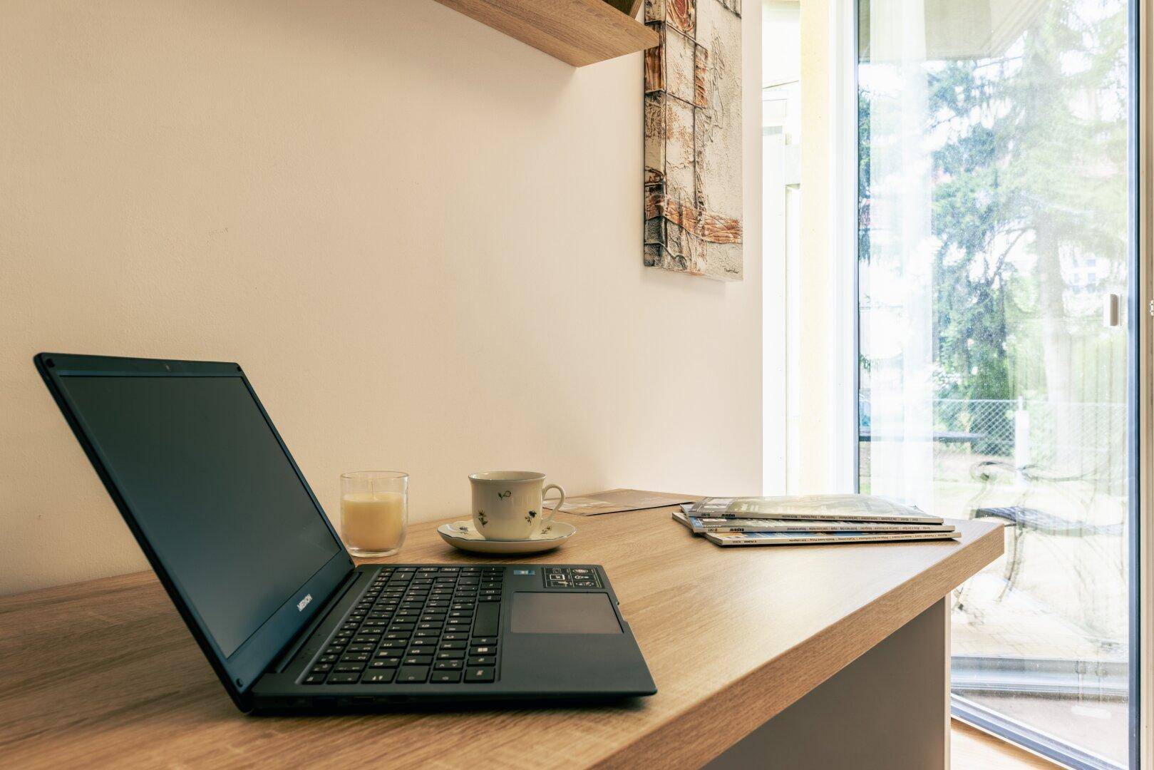 Arbeitsplatz mit Laptop und Blick ins Grüne durch das große Fenster, ideal für Home-Office.