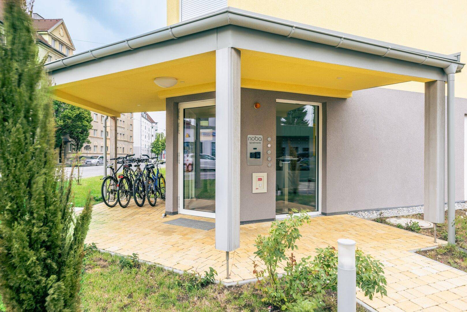 Eingangsbereich des Gebäudes mit Überdachung und Fahrradabstellplätzen, modern und einladend.