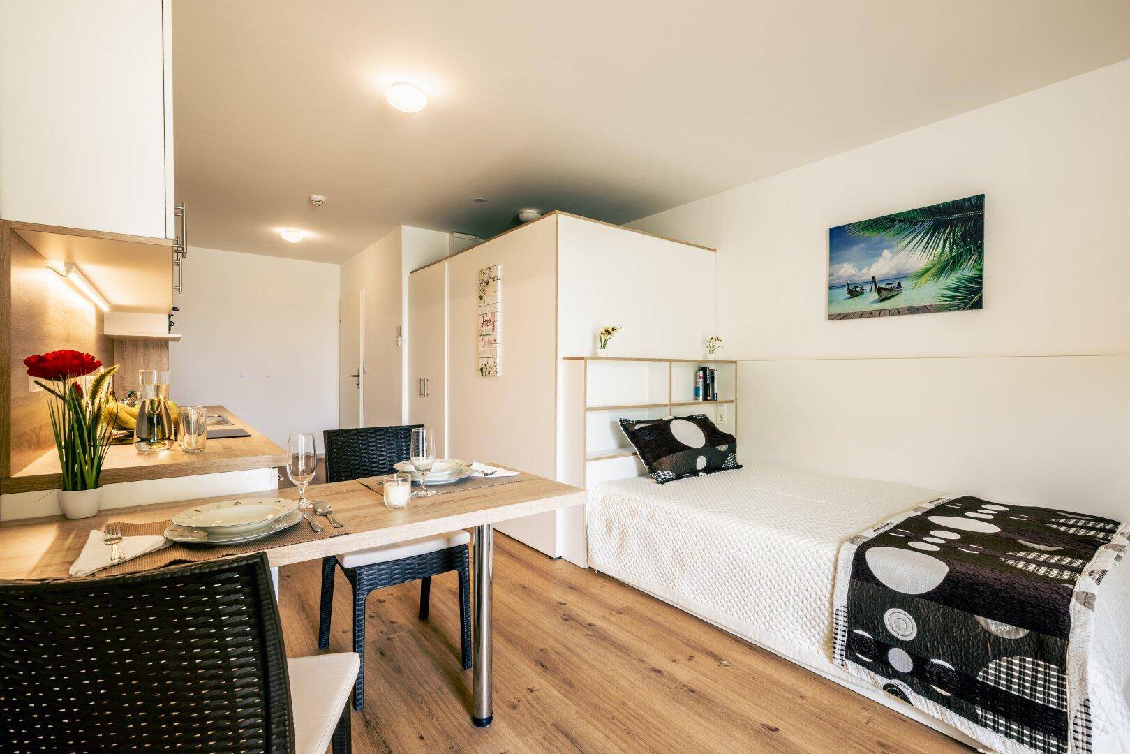 Helles Studio-Apartment mit Schlafbereich, Esstisch und funktionaler Küchenzeile.