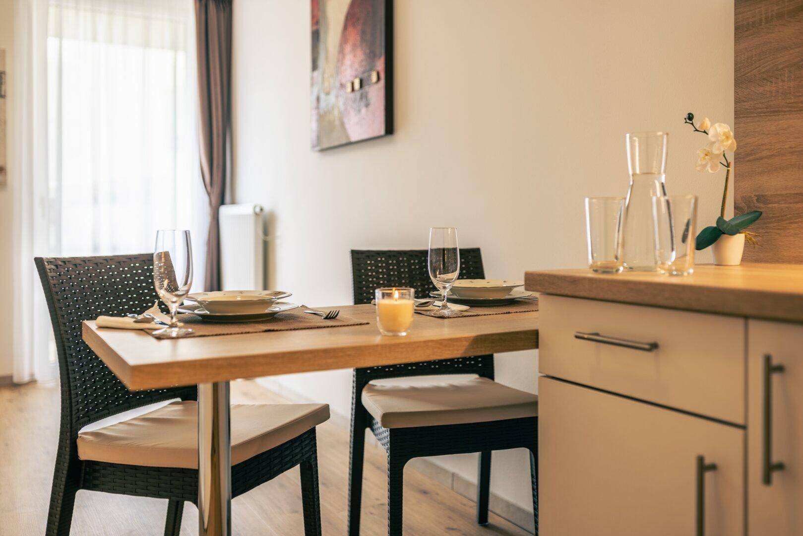 Gedeckter Esstisch für zwei Personen neben der Küchenzeile in einem hellen Studio-Apartment.