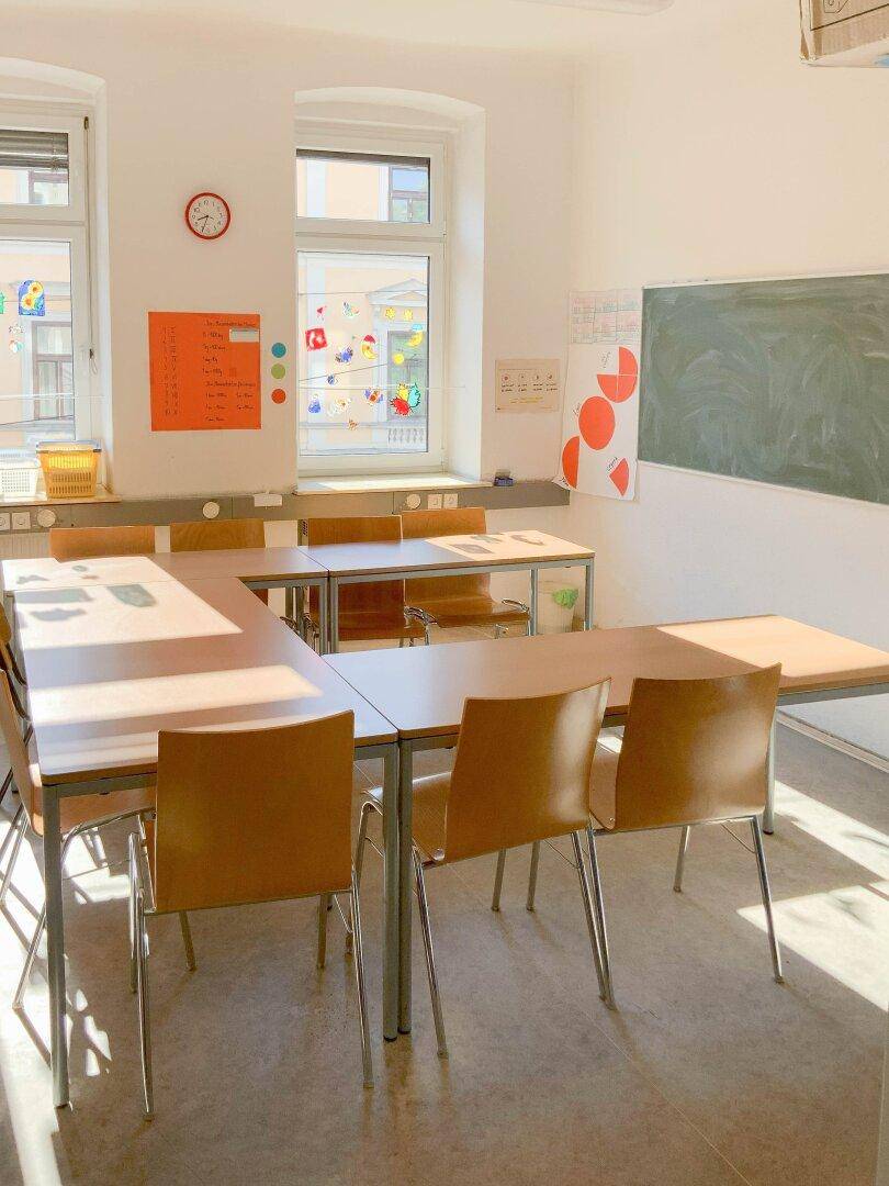 Freundlicher Unterrichtsraum mit Tafel und großen Fenstern, die viel Licht hereinlassen.