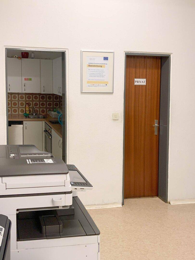 Kleine Küchenzeile mit Spüle und Schränken, sichtbar durch eine Türöffnung.
