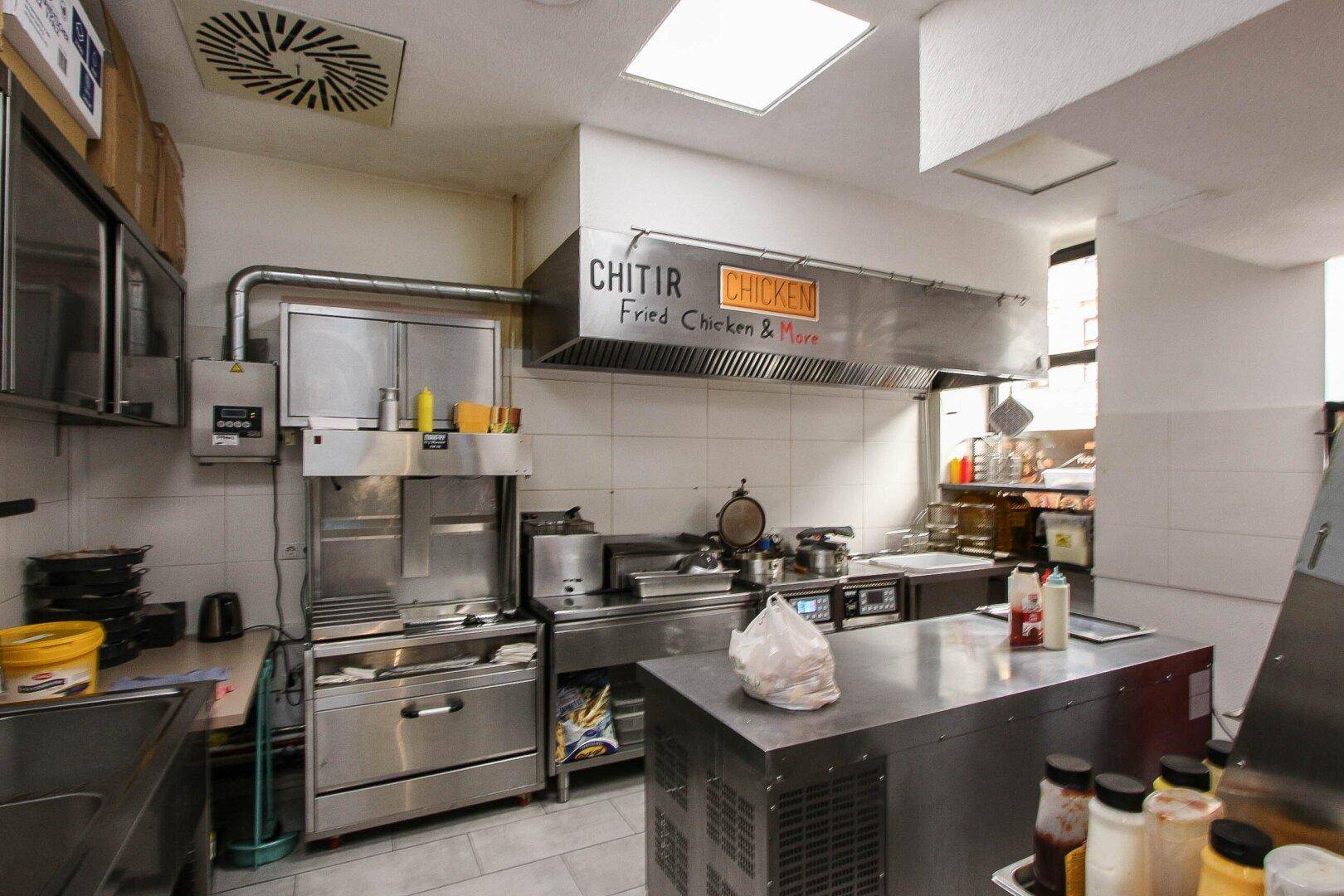 Professionelle Gewerbeküche mit Edelstahlgeräten, großer Dunstabzugshaube und gefliesten Wänden für einfache Reinigung.