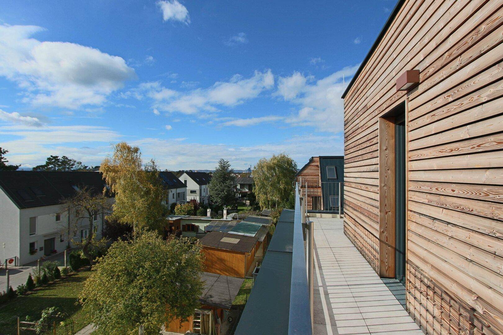 Langer Balkon mit Holzfassade und weitem Blick über die grüne Umgebung.