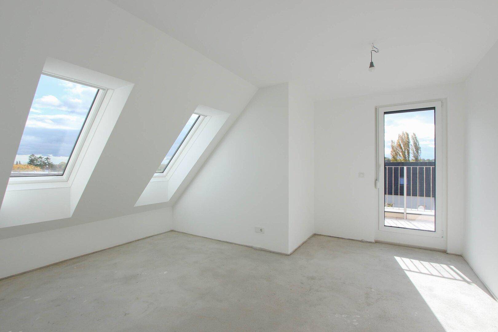 Rohbau eines hellen Dachgeschosszimmers mit Dachfenstern und Balkonzugang.