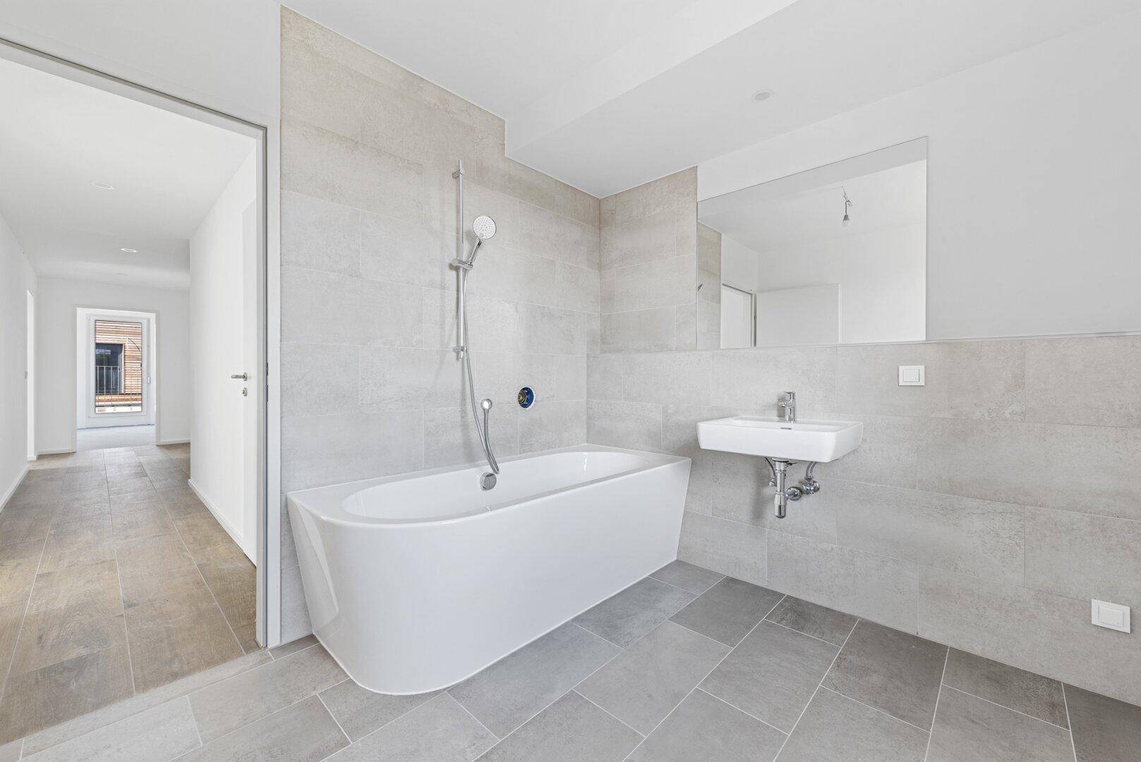 Modernes Badezimmer mit Badewanne, Einzelwaschbecken und großen Fliesen.