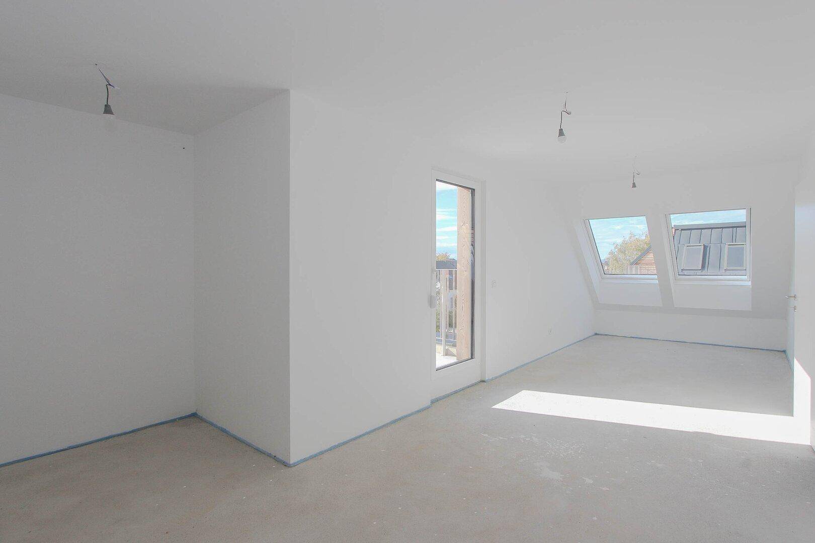Rohbau eines hellen Dachgeschosszimmers mit großen Fenstern und Zugang zum Balkon.