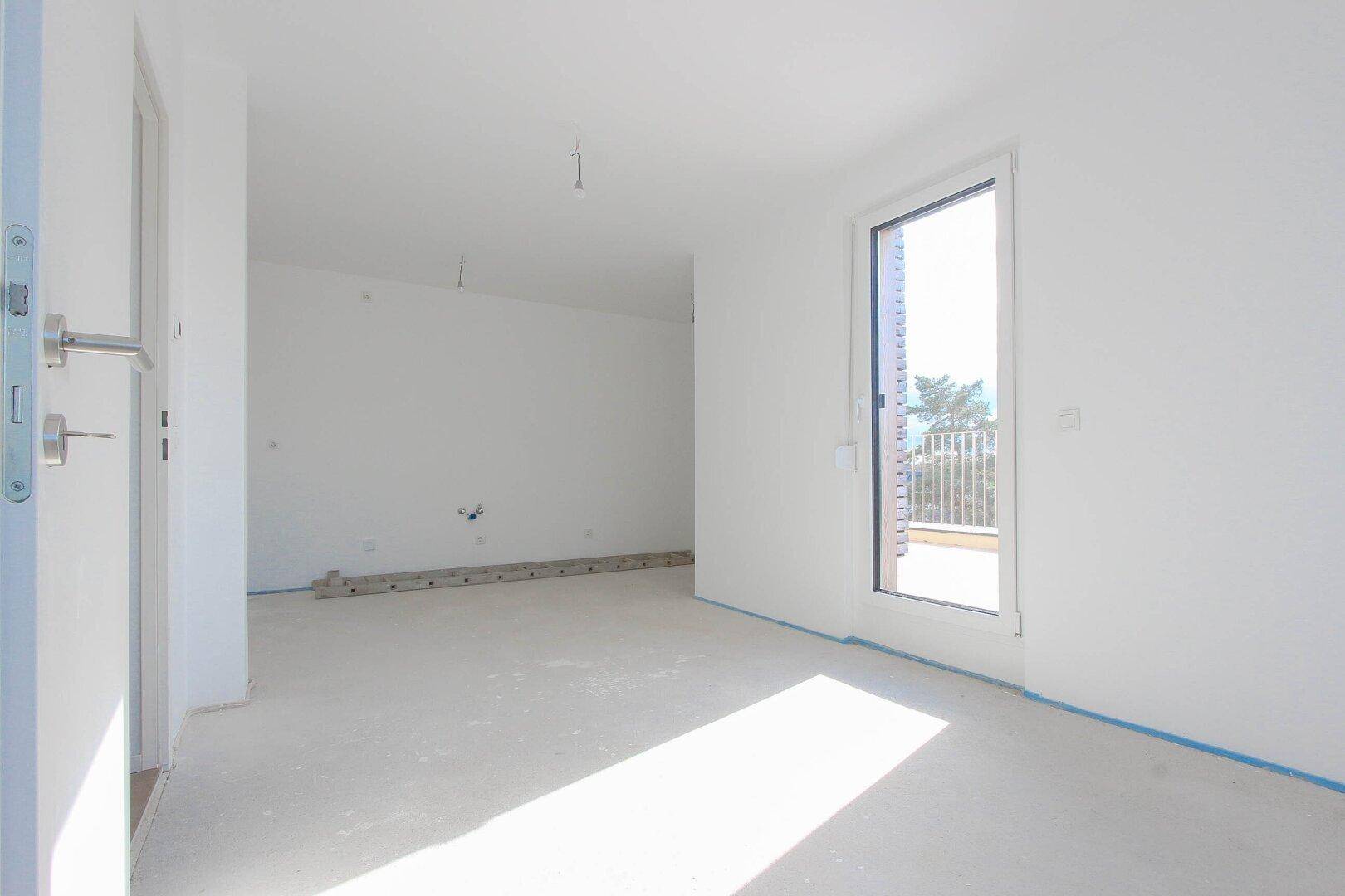 Rohbau einer Küche mit weißen Schränken und Zugang zu einem sonnigen Balkon.