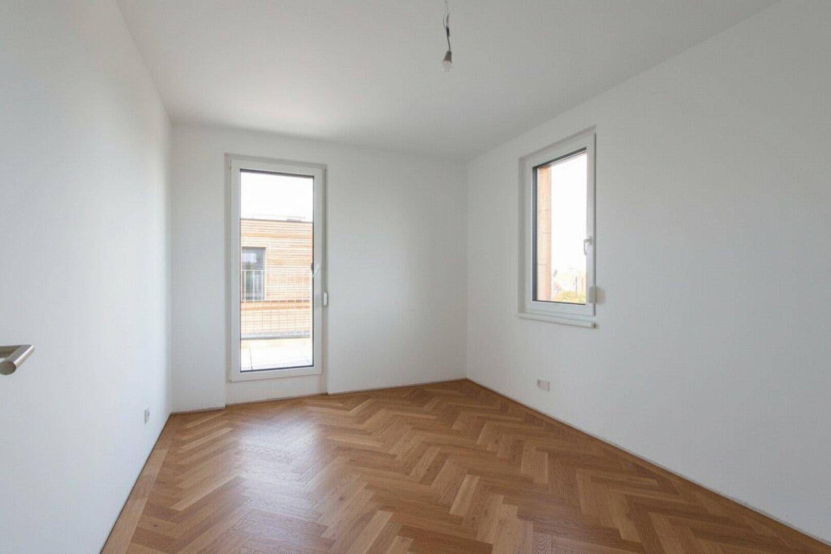 Helles Zimmer mit Parkettboden und Zugang zu einem Balkon, ideal als Schlafzimmer.