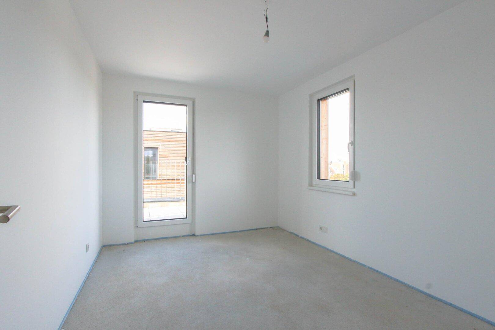 Rohbau eines hellen Zimmers mit Fenster und Zugang zu einem Balkon.