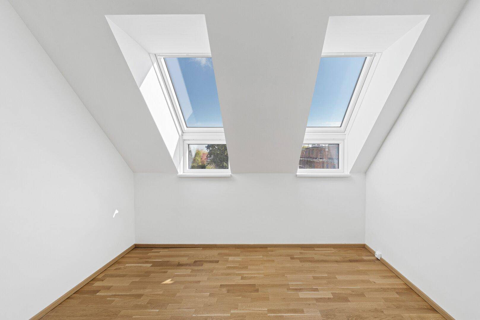 Helles Dachzimmer mit Holzboden, schrägen Wänden und zwei großen Dachfenstern.