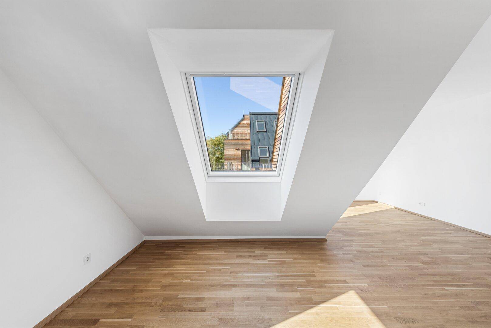 Lichtdurchfluteter Raum im Dachgeschoss mit Holzboden und großem Dachfenster.