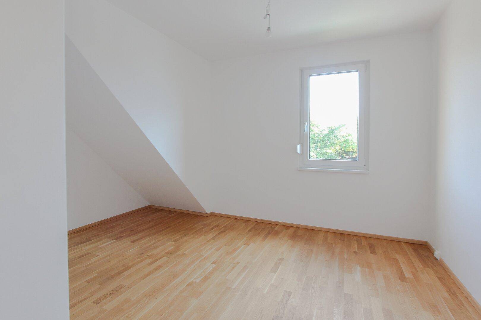 Helles Schlafzimmer im Dachgeschoss mit Parkettboden und einem Fenster.