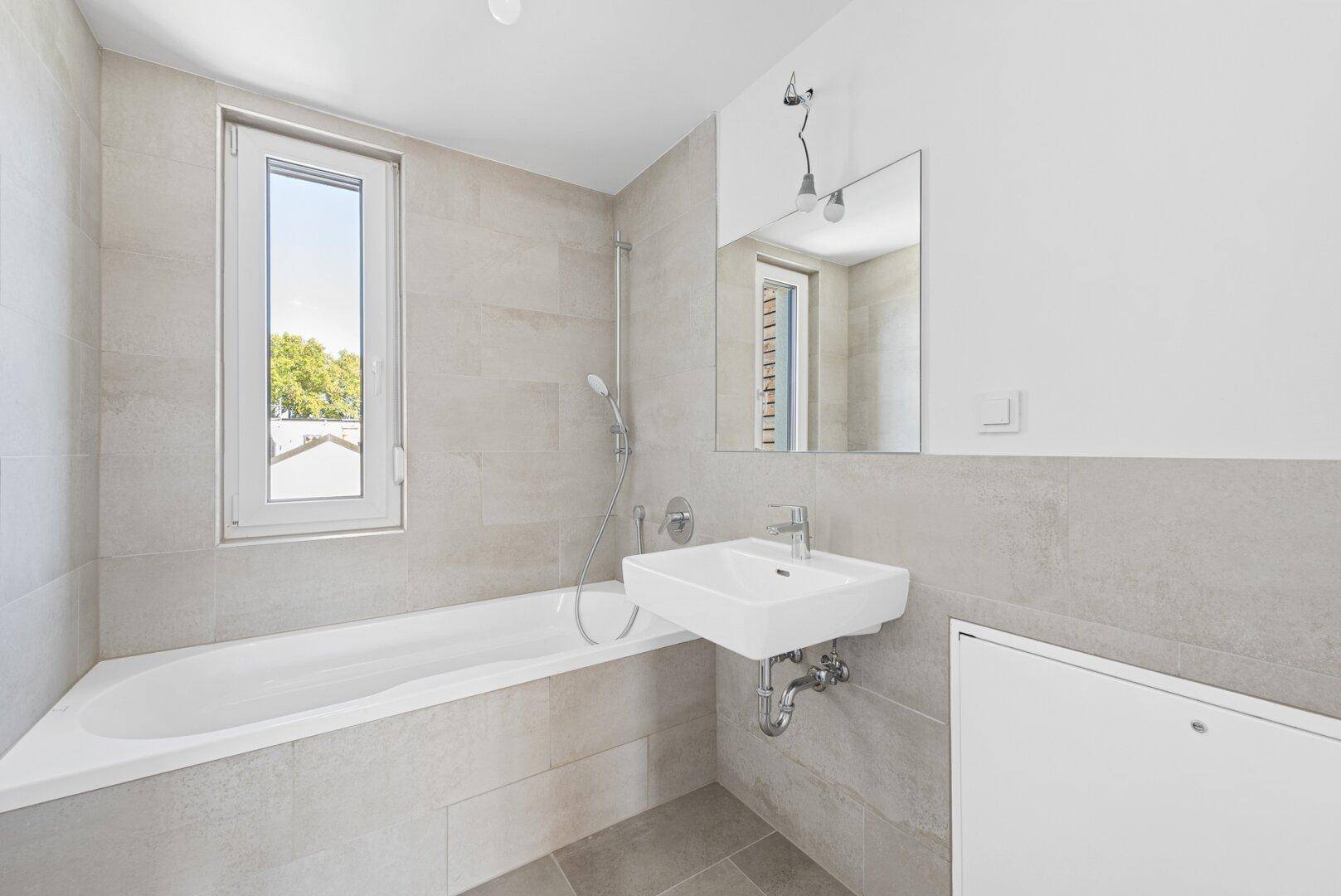 Modernes Badezimmer mit Badewanne, Waschbecken und einem Fenster für Tageslicht.