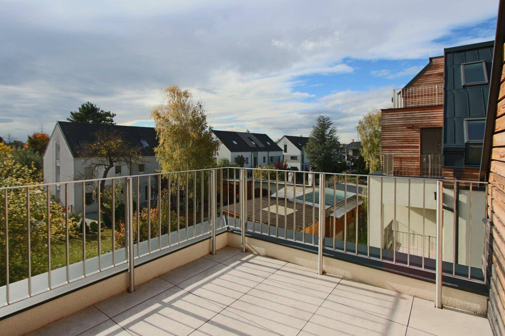Geräumiger Balkon mit Fliesenboden und Blick auf die umliegenden Häuser und Grünflächen.