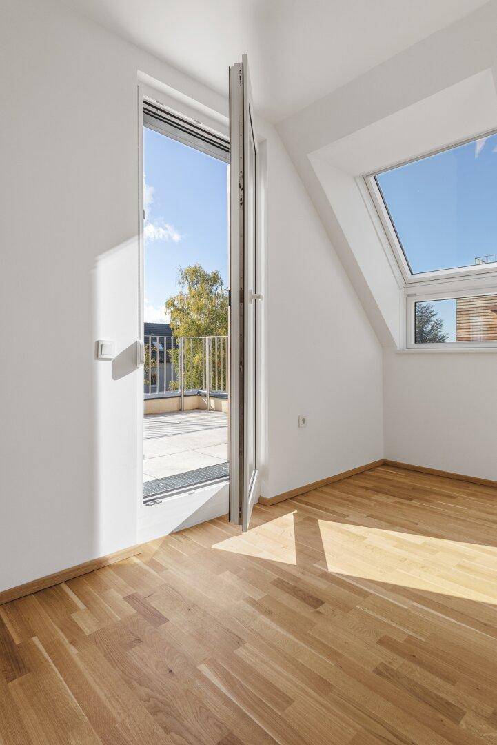 Lichtdurchfluteter Raum mit Holzboden und offener Balkontür, die den Blick nach draußen freigibt.