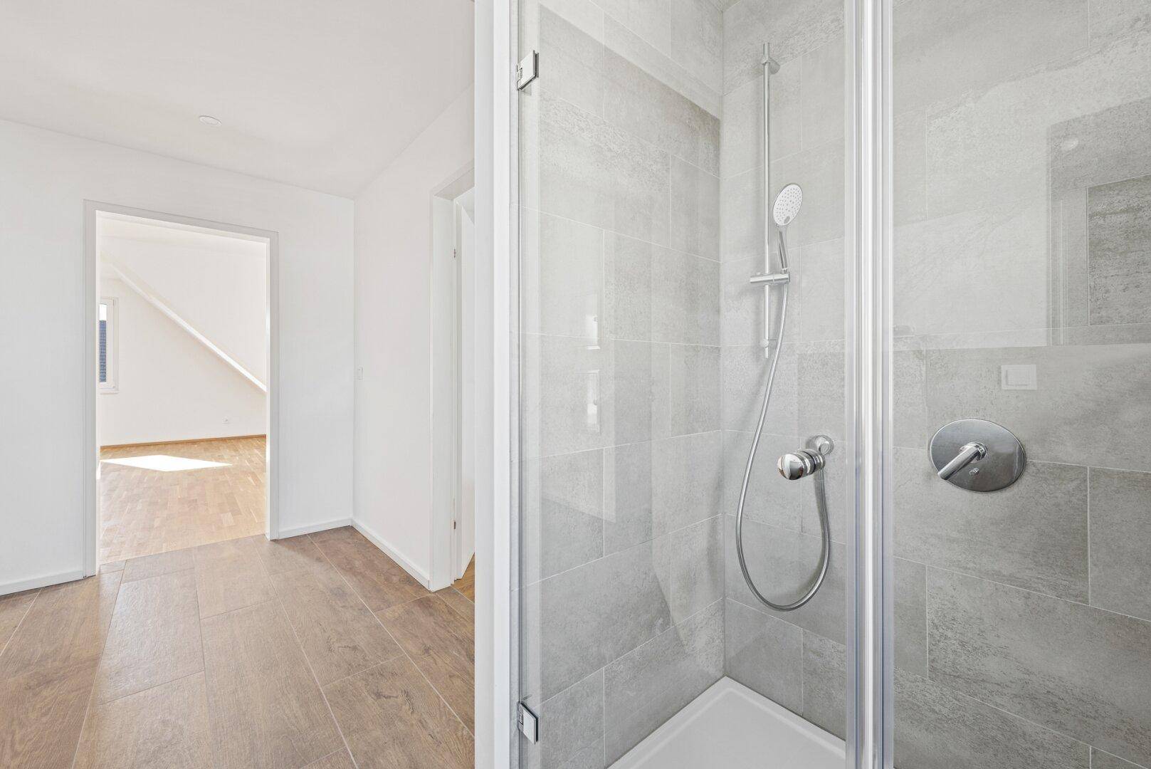 Duschbereich in einem modernen Badezimmer mit Glaswand und Blick in den angrenzenden Flur.