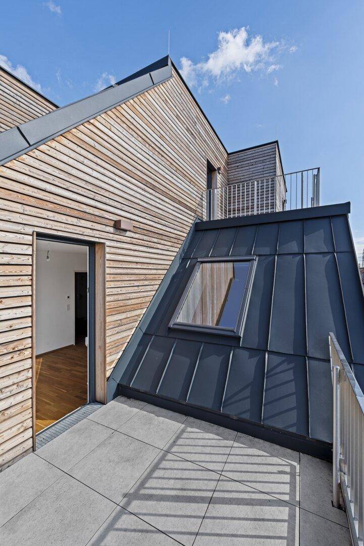 Moderner Balkon mit Holzfassade und Metallgeländer, bietet Zugang zu einem hellen Innenraum.