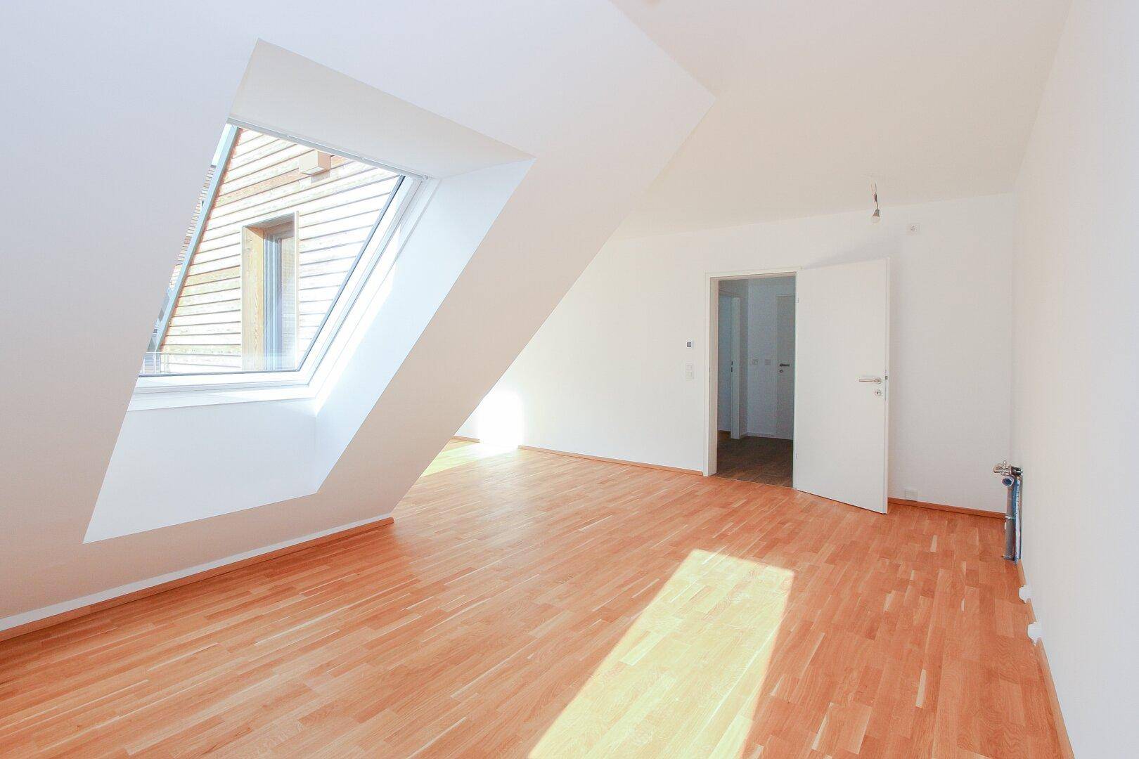 Heller Raum im Dachgeschoss mit Holzboden und großem Dachfenster, das viel Licht hereinlässt.