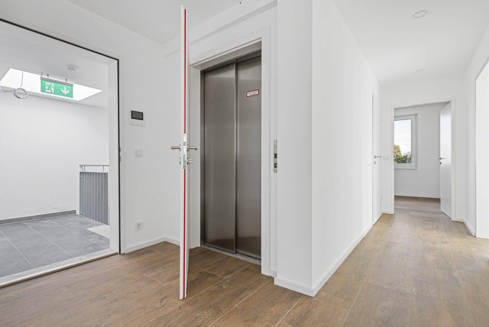 Heller Flur mit modernem Aufzug und Holzoptik-Fliesenboden im Neubau.