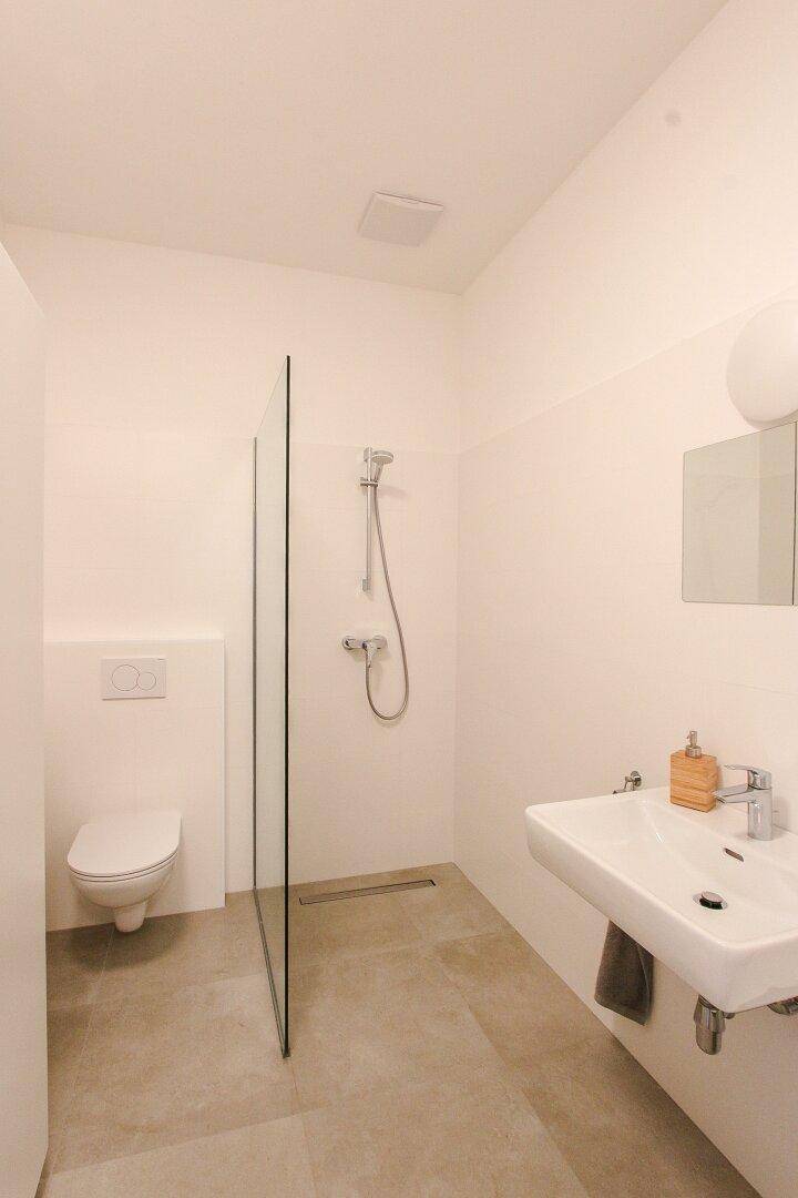 Modernes Badezimmer mit ebenerdiger Dusche, wandhängendem WC und Einzelwaschbecken.