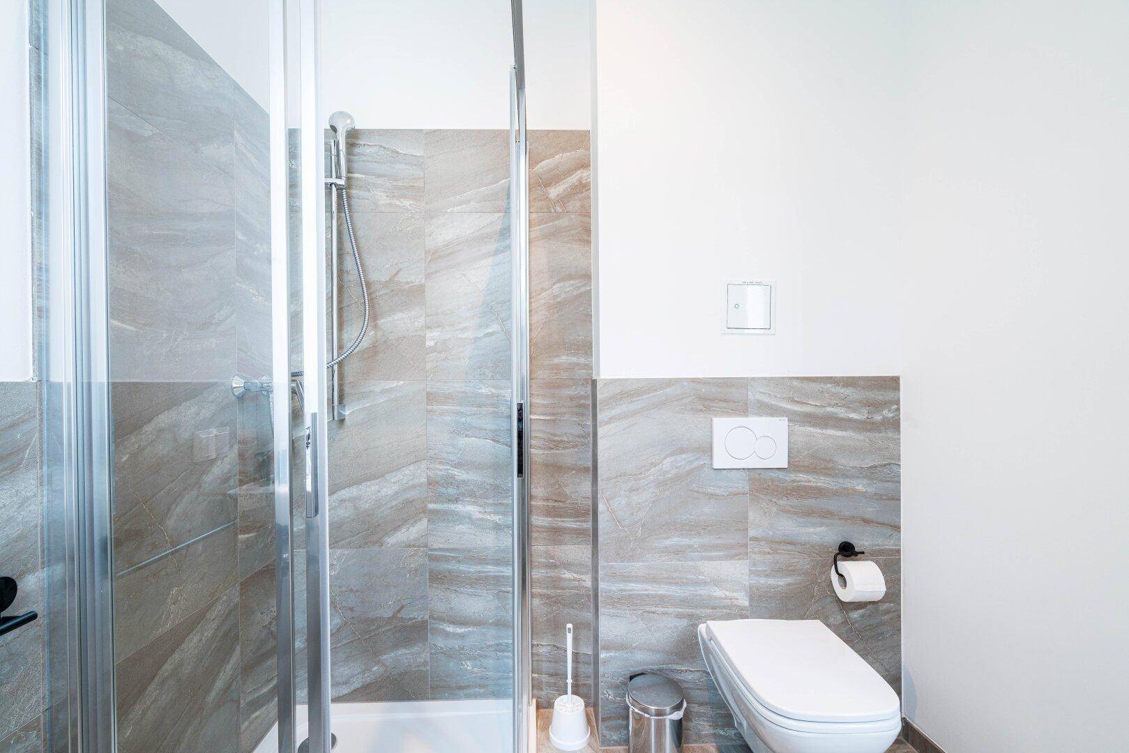 Modernes Badezimmer mit Duschkabine, wandhängendem WC und eleganten grauen Fliesen.