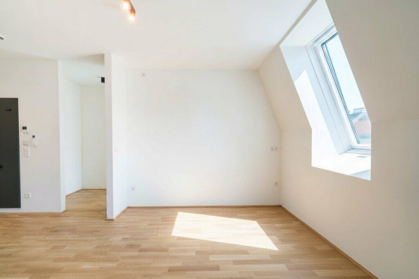 Lichtdurchfluteter Raum mit Dachschräge, Holzfußboden und modernen Deckenleuchten.