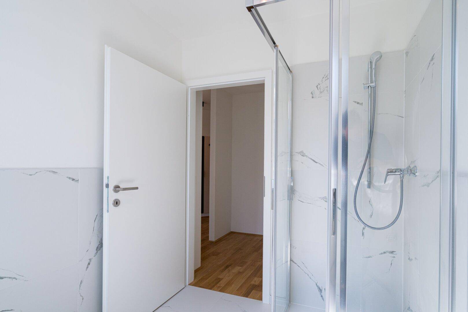 Modernes Badezimmer mit Duschkabine und eleganten Marmorfliesen an den Wänden.