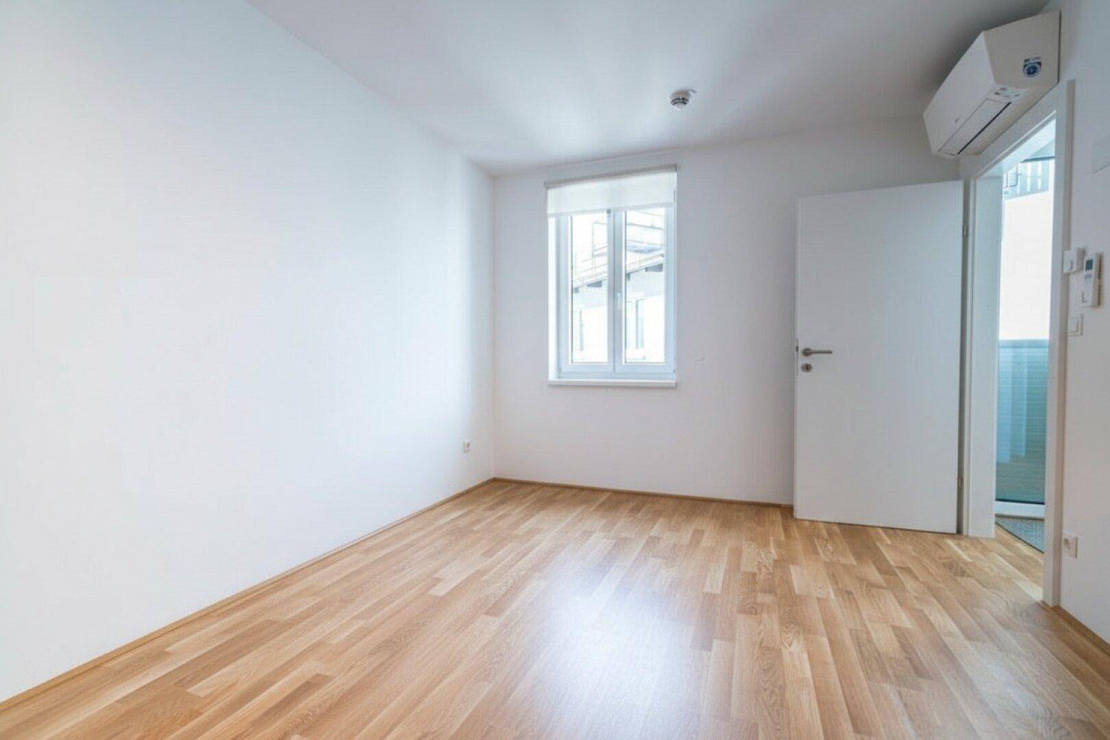 Helles Schlafzimmer mit Holzboden, weiß gestrichenen Wänden und Klimaanlage für Komfort.