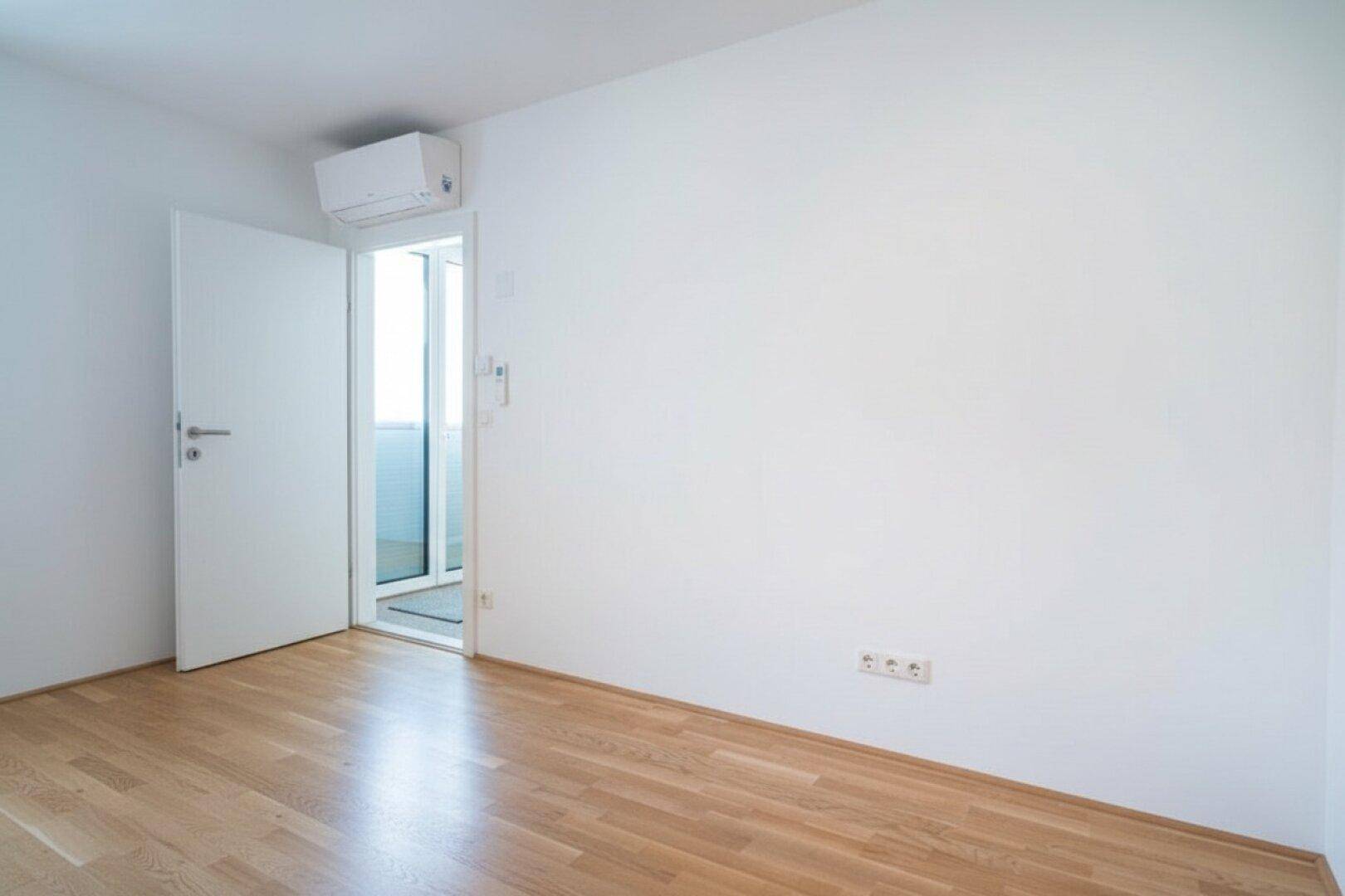 Geräumiges Schlafzimmer mit Holzboden, weißer Wandgestaltung und Zugang zu einem Außenbereich.