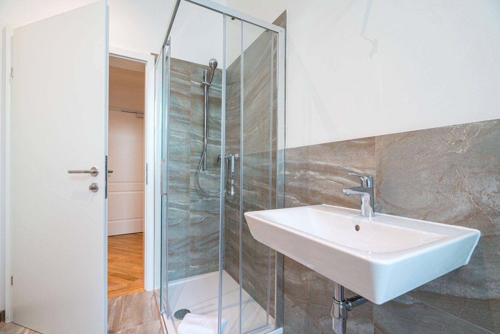 Modernes Badezimmer mit Duschkabine, Waschbecken und grauen Fliesen.