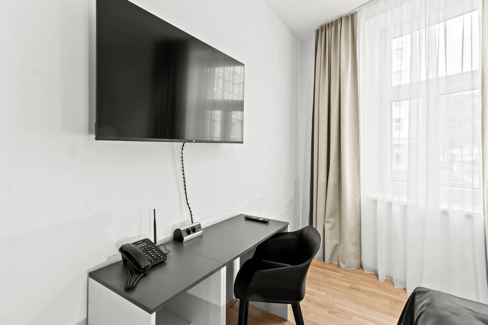 Arbeitsbereich mit Schreibtisch, Stuhl und wandmontiertem Fernseher neben dem Fenster.