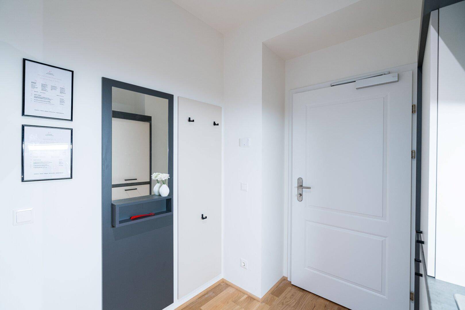 Heller Eingangsbereich mit Garderobe, Spiegel und Holzboden.