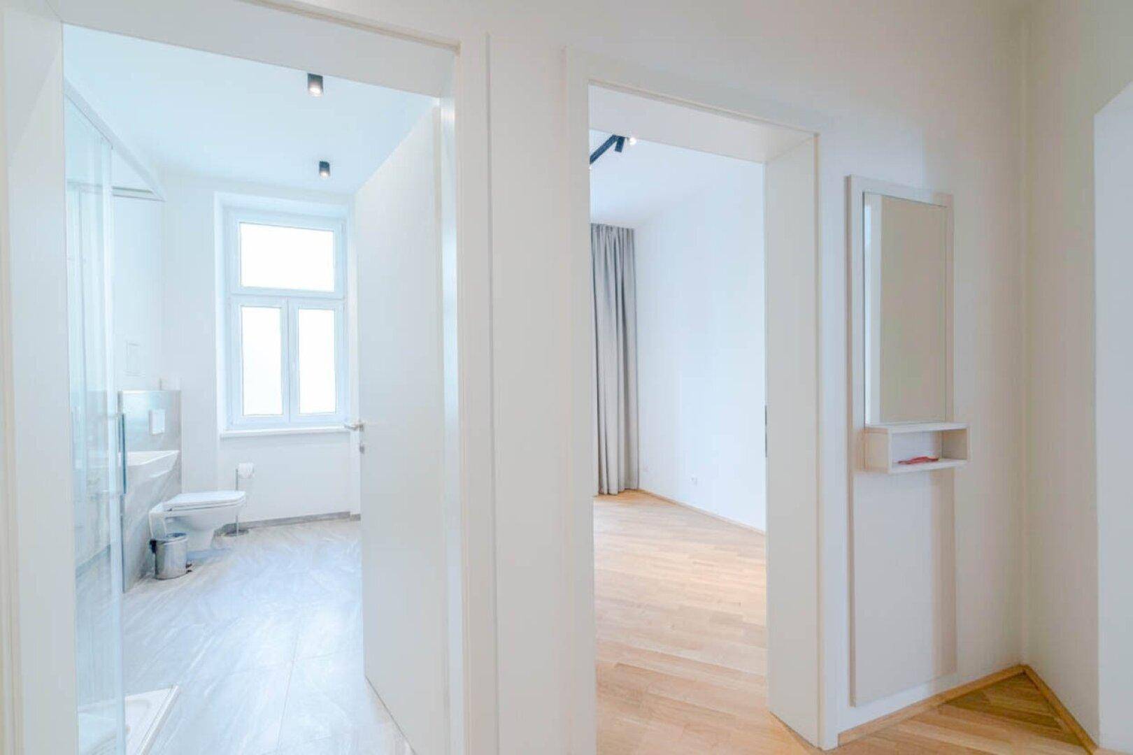 Heller Flur mit Blick in ein Badezimmer und ein weiteres Zimmer.