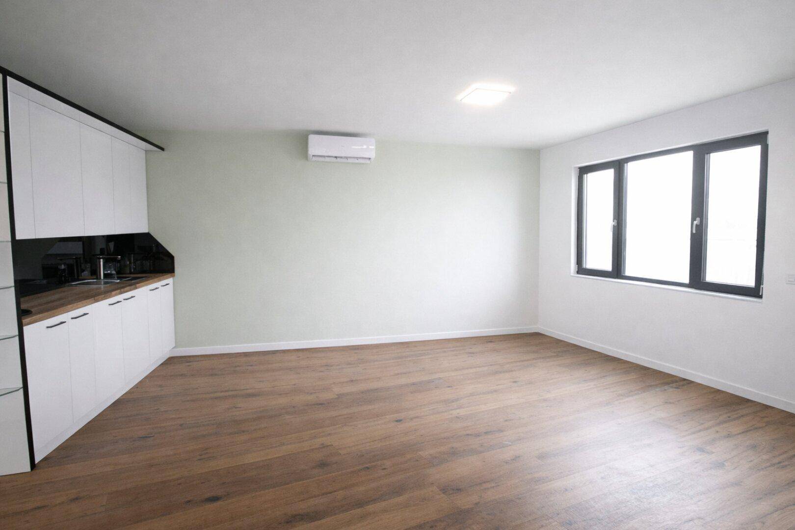 Heller Wohnraum mit Holzboden, einer modernen Küchenzeile und einem Fenster, das viel Licht spendet.