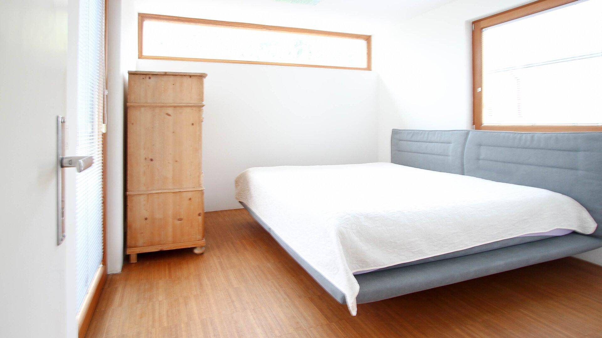 Ruhiges Schlafzimmer mit Doppelbett, Holzboden und viel natürlichem Tageslicht.